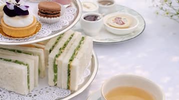 Ein Tisch ist gedeckt mit Sandwiches, Gebäck und einer Tasse Tee.