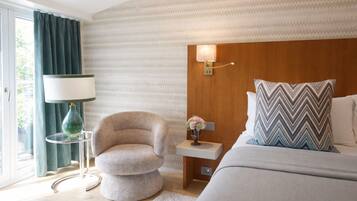 A modern hotel room with a bed, a chair, a nightstand, a lamp, and a wall-mounted light fixture.