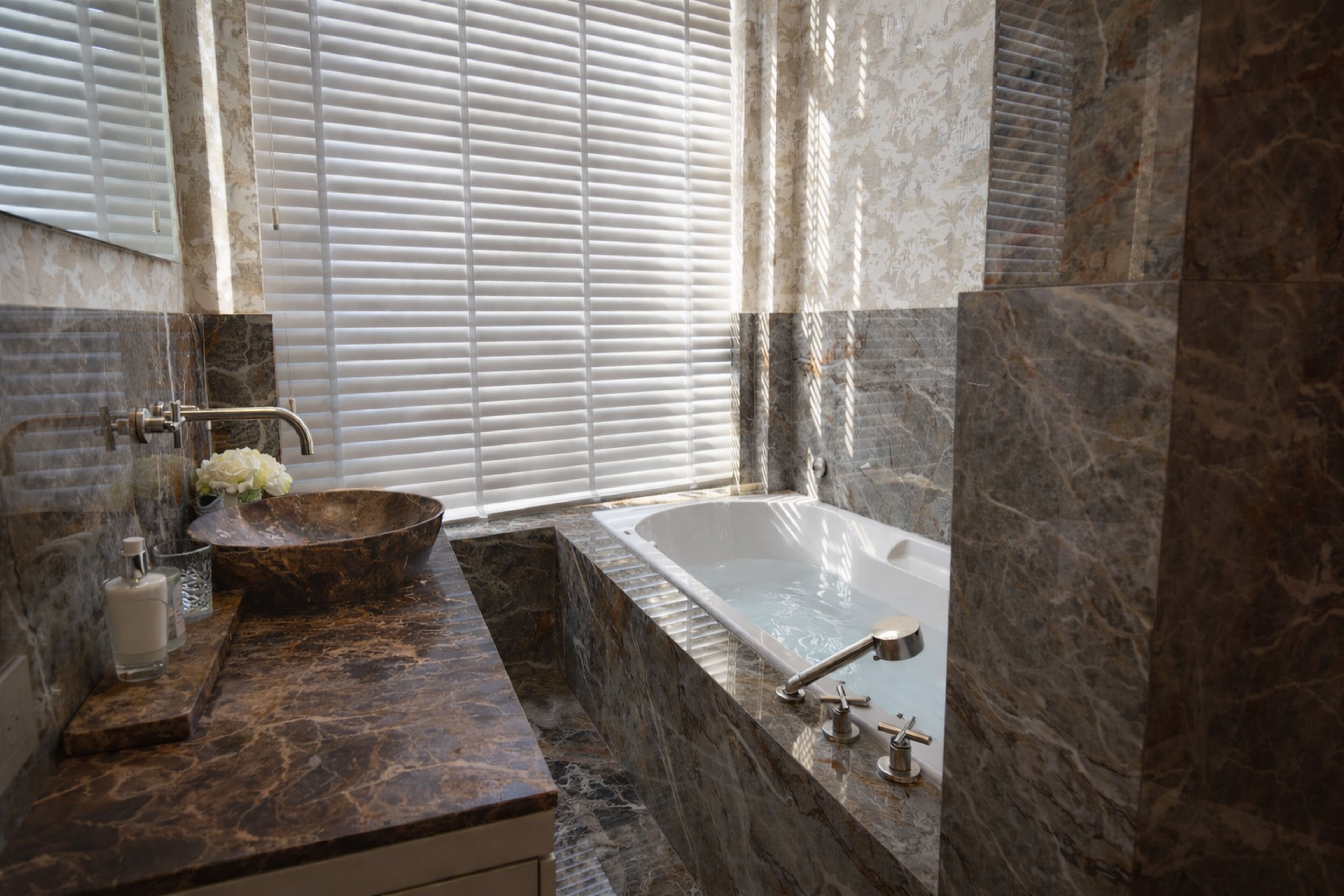 A bathroom with a marble sink, a bathtub, and a window with blinds.