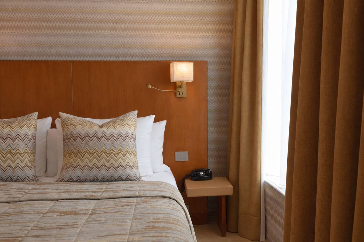 A hotel room with a large bed, a nightstand with a lamp, and a window with curtains.
