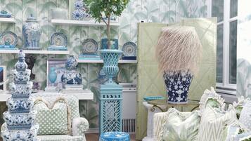 A room with a patterned wallpaper, a variety of blue and white vases, a green upholstered chair, and a large vase with a textured design.