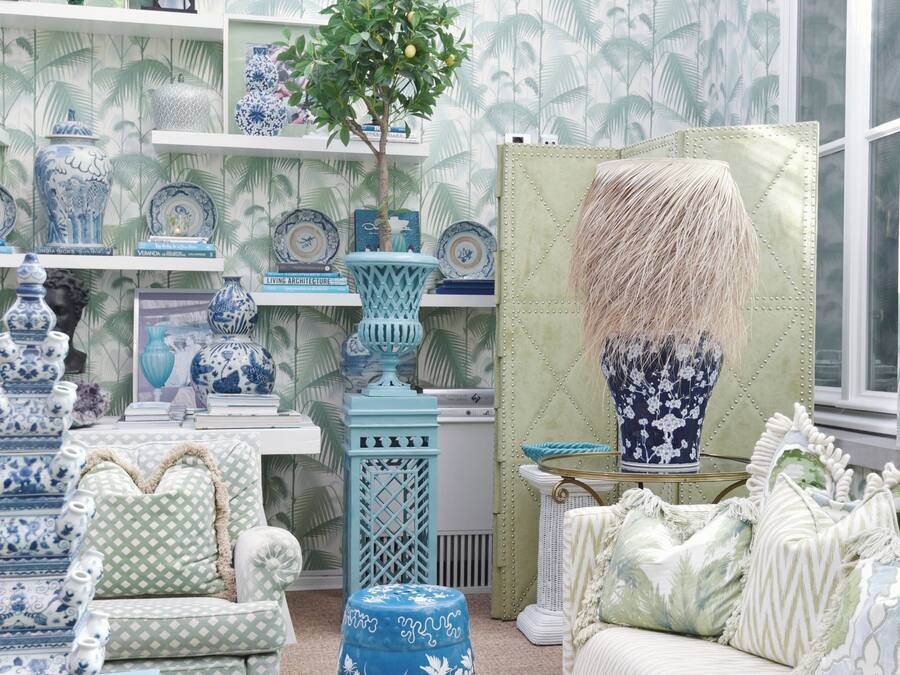 A room with a patterned wallpaper, a variety of blue and white vases, a green upholstered chair, and a large vase with a textured design.