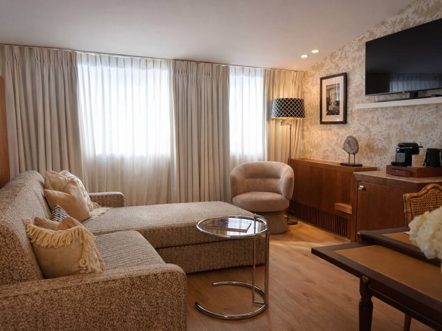 A living room with a sofa, armchair, coffee table, and a flat-screen TV mounted on the wall.