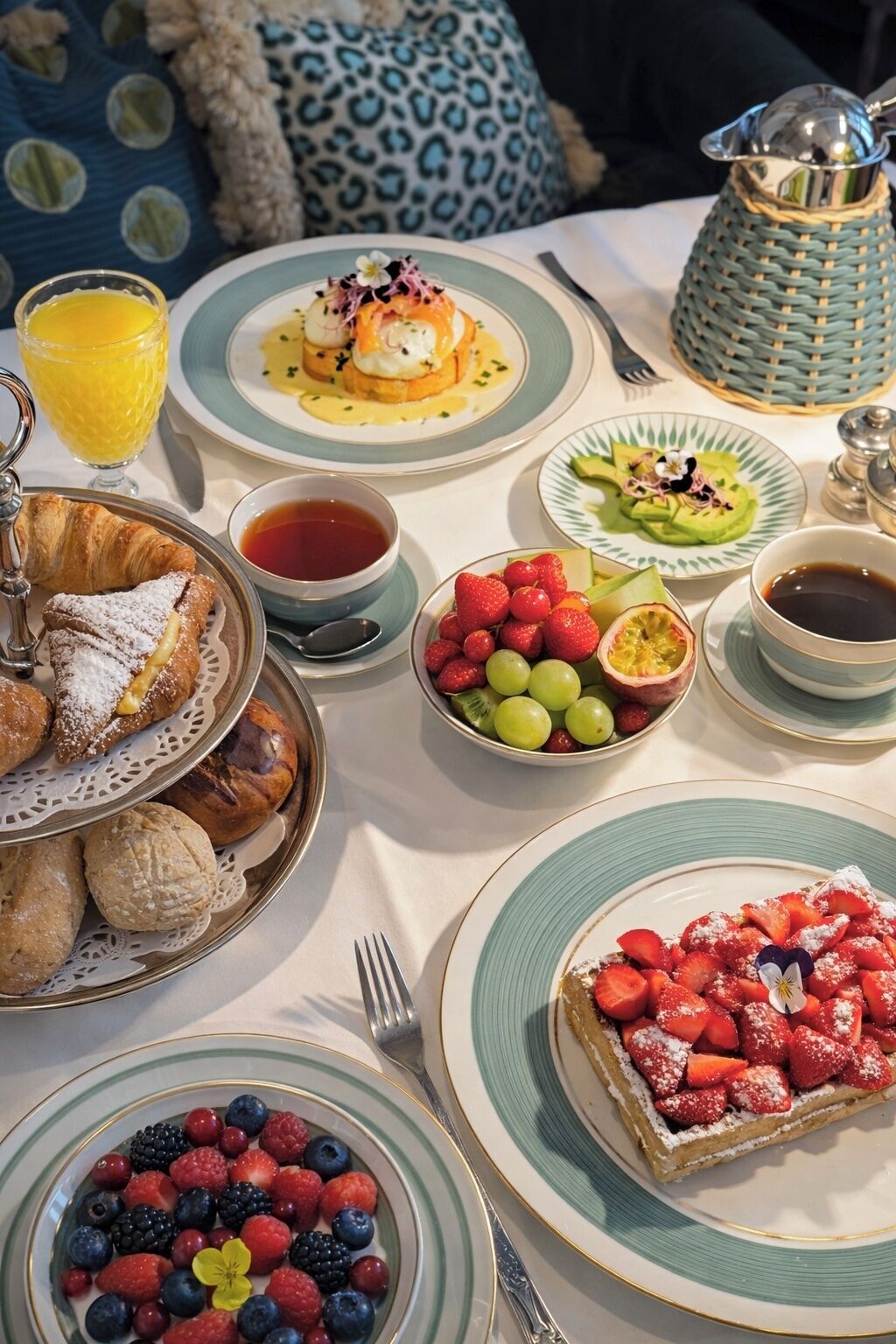 Une table dressée pour le petit-déjeuner, avec divers plats, notamment des viennoiseries, des fruits et des boissons.