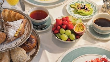 Une table dressée pour le petit-déjeuner, avec divers plats, notamment des viennoiseries, des fruits et des boissons.