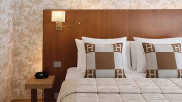 A hotel room with a wooden headboard, a bedside lamp, a telephone, and a bed with pillows featuring a checkered pattern.