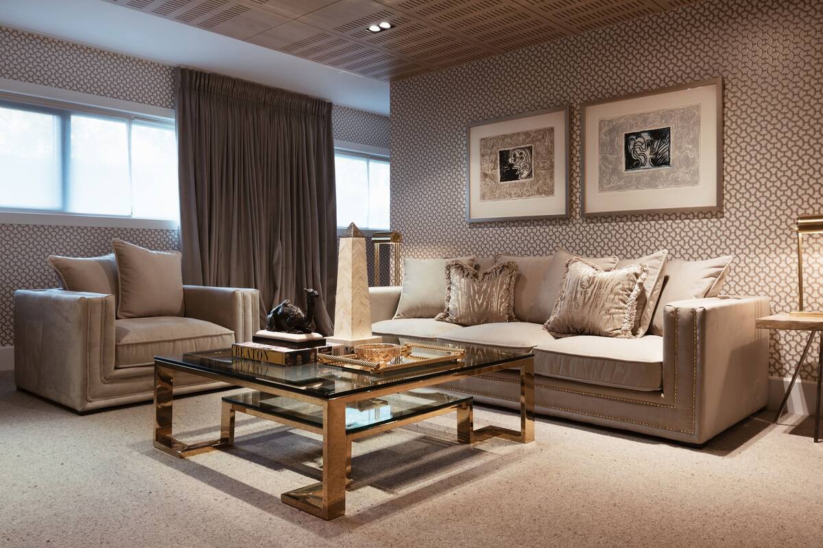 A modern living room with a beige sofa, a glass coffee table, and a patterned wall.