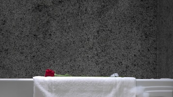 A bathroom with a granite wall, a white bathtub, and a towel rack with a white towel.