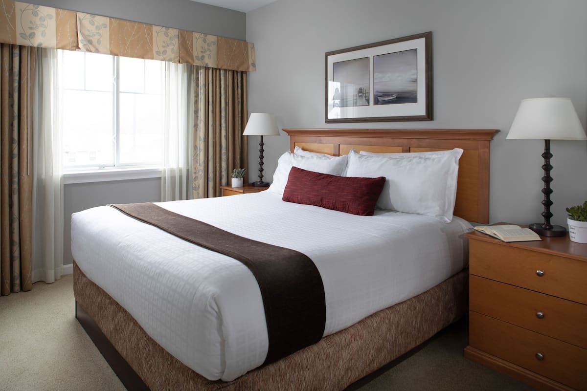 A neatly made bed with a wooden headboard, two bedside lamps, and a framed picture above the headboard.