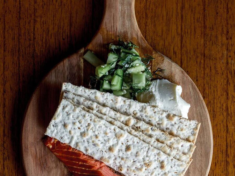 Una tabla de madera con salmón, queso blanco y una ensalada de pepino.