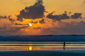 Un atardecer sobre el océano, con una persona caminando por la playa.