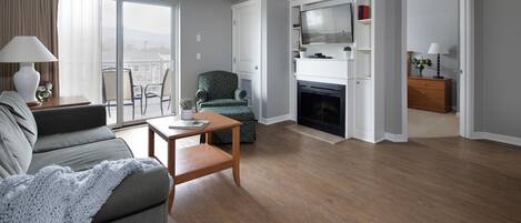A modern living room with a sofa, a coffee table, a fireplace, and a balcony with a view.