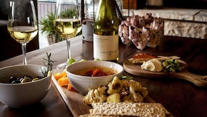 A wooden table with a bottle of wine, glasses, bowls of food, and a rustic stone fireplace in the background.