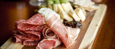 A wooden board with various cured meats, cheeses, and grapes, accompanied by a bottle of wine and a glass.