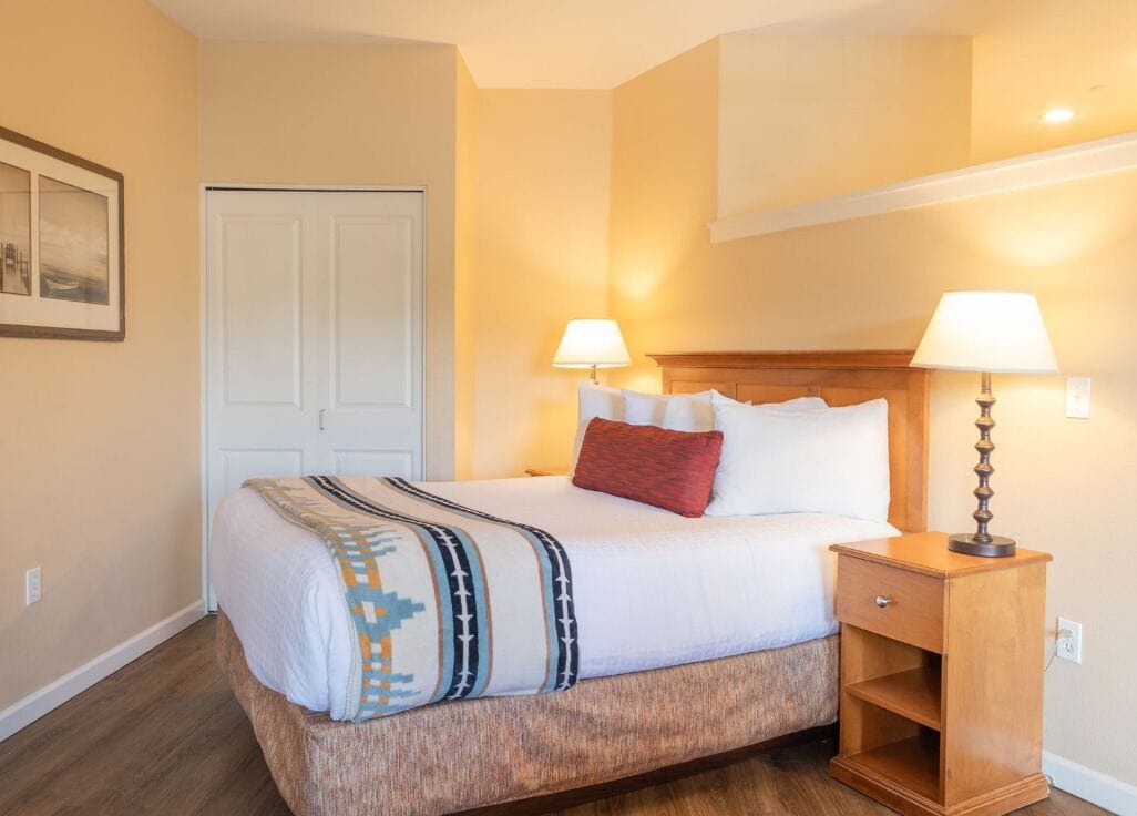 Ein Hotelzimmer mit einem Bett, Nachttischlampen, einem Holfnachtkästchen und einer Tür.