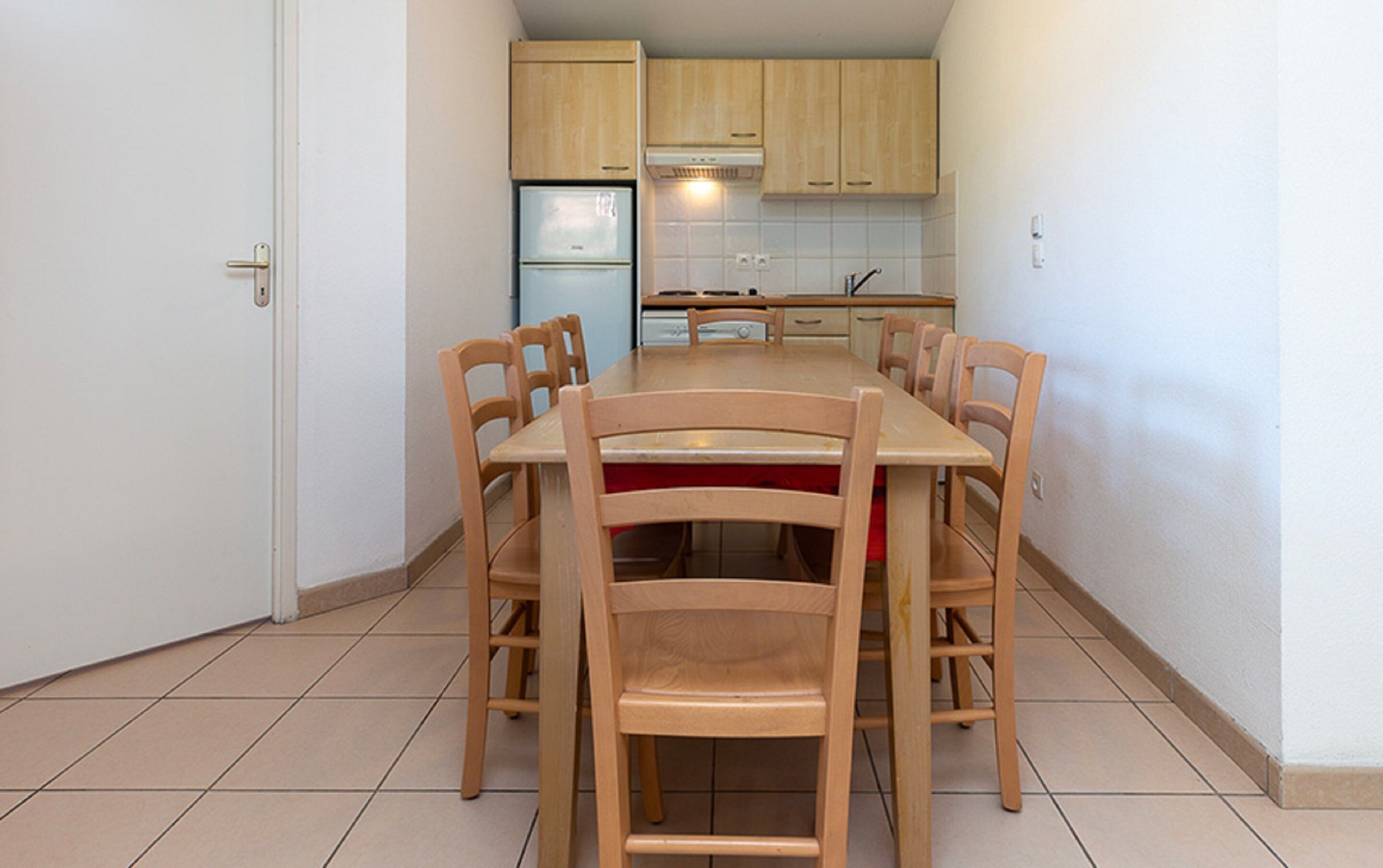 A compact kitchen with wooden cabinets, a built-in oven, and a dining table with chairs.
