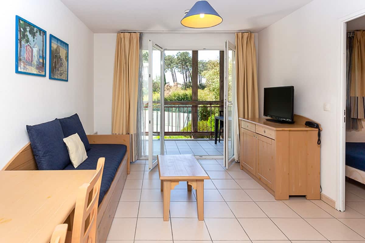 A compact living space with a sofa, a small table, a TV, and a sliding door leading to an outdoor area.