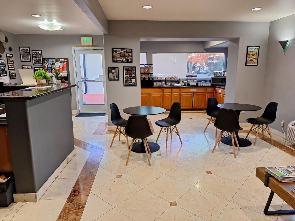 A hotel lobby with a reception desk, a seating area with round tables and chairs, a kitchen area, and framed pictures on the walls.