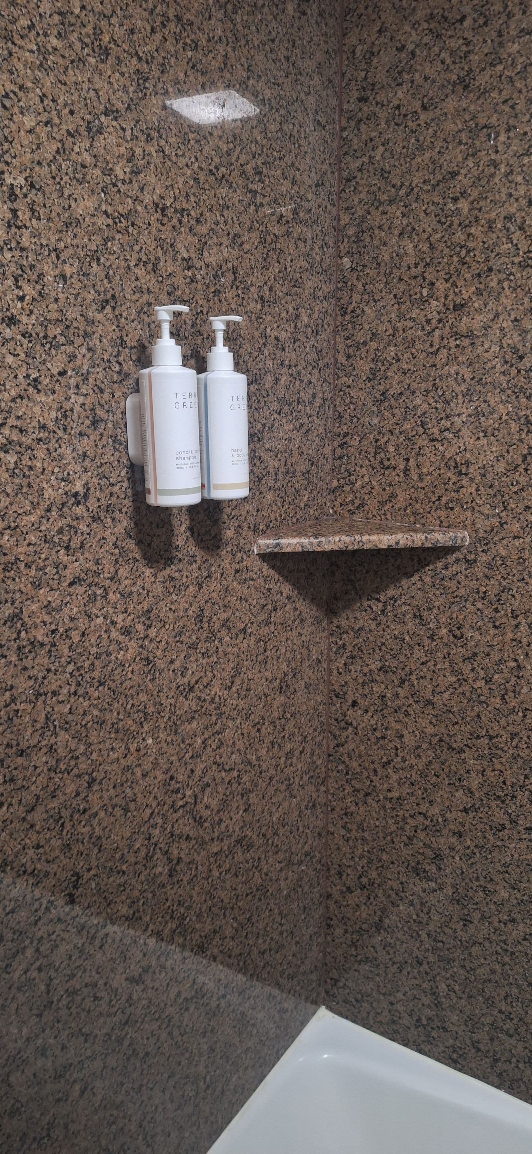 A bathroom with a granite wall, a white bathtub, and two white bottles of hand and body wash on a shelf.