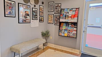 Zona de recepción con un banco, fotos enmarcadas, un tablón de anuncios con folletos turísticos y una puerta con un cartel de 'No Estacionar'.