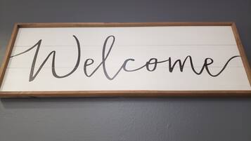 Une pancarte d’accueil encadrée, avec le mot « Bienvenue » écrit en lettres cursives sur un fond blanc.