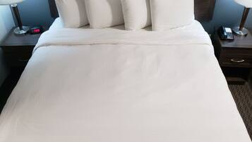 Una cama bien hecha con ropa blanca, un cabecero de madera y dos mesitas de noche con lámparas y un teléfono.