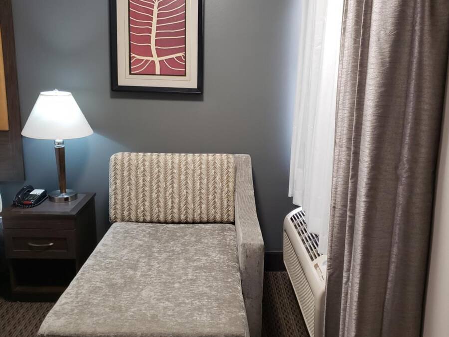 Habitación de hotel con cama, mesita de noche con lámpara, un cuadro en la pared y ventana con cortinas.