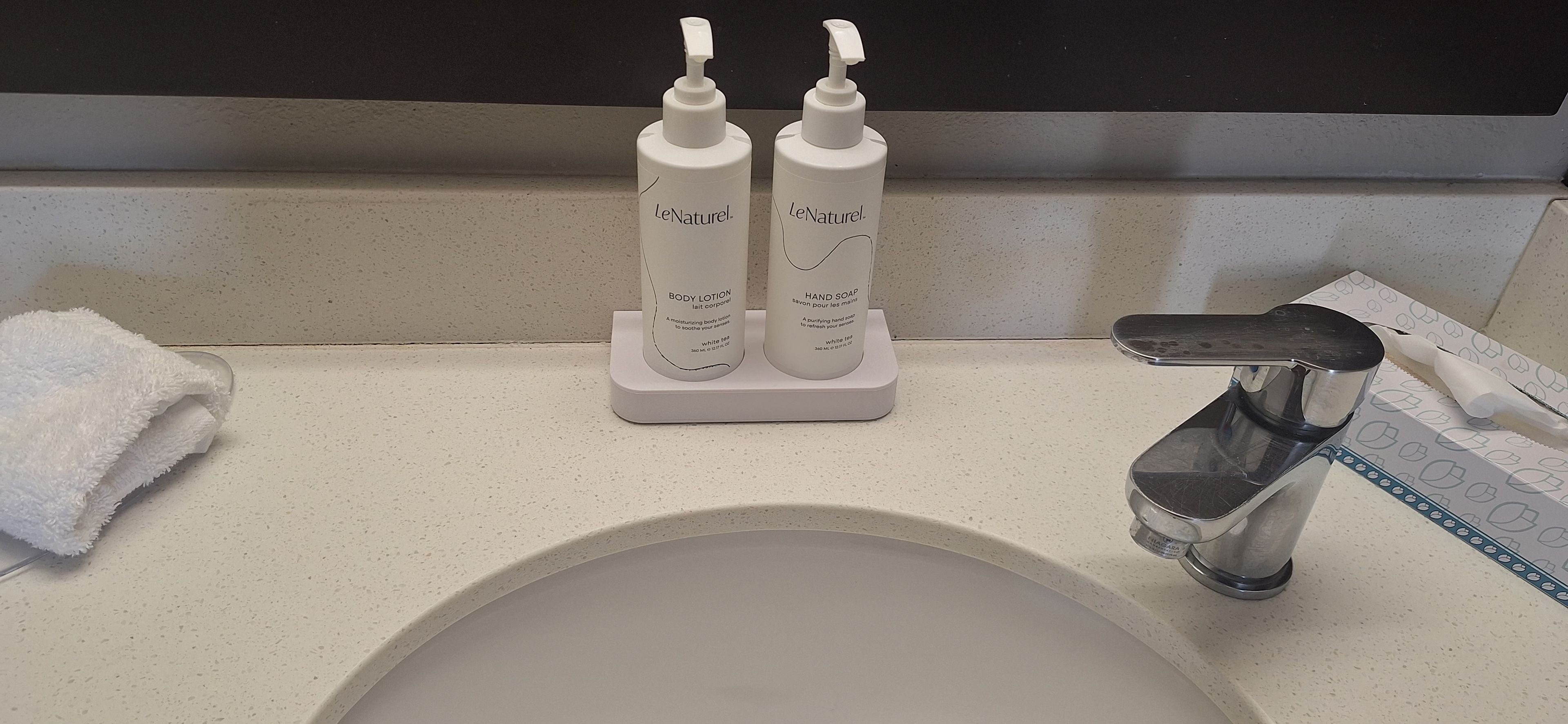A bathroom sink with two bottles of LeNaturel body lotion and hand soap on a soap dish.