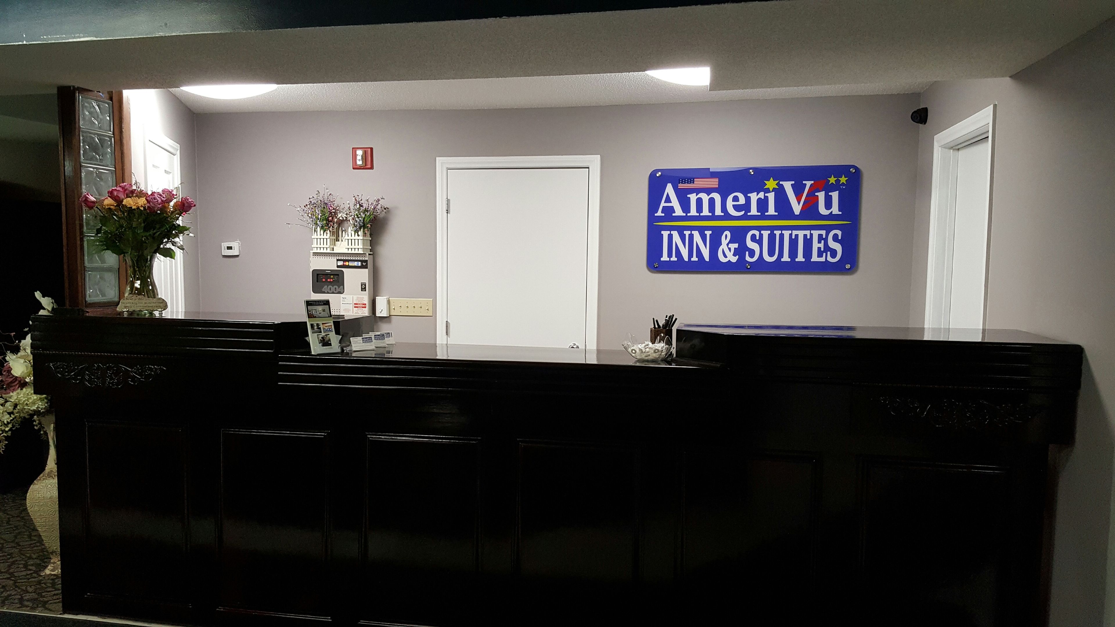 Una mesa de recepción con un cartel de AmeriViu Inn & Suites, una puerta blanca, una planta pequeña y un detector de incendios.