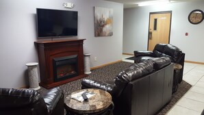 A living room with a fireplace, leather sofa, and a flat-screen TV. - Amerivu Inn And Suites New Richmond (New Richmond)