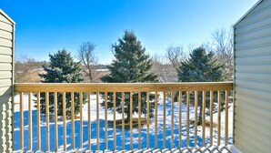 A wooden deck with a railing, a snow-covered yard, and evergreen trees in the background. - Amerivu Inn And Suites New Richmond (New Richmond)