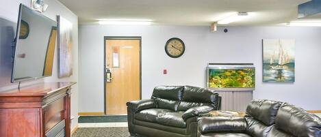 A living room with a brown leather sofa, a wooden coffee table, a flat-screen TV, a fish tank, and artwork on the walls.