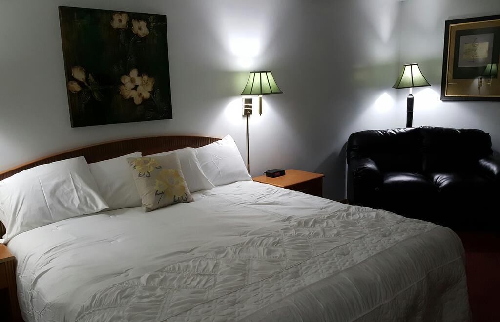 A hotel room with a large bed, two bedside lamps, a black leather chair, and a floral painting on the wall.