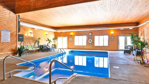 An indoor swimming pool with a wooden ceiling and walls, surrounded by lounge chairs and potted plants. - Amerivu Inn And Suites New Richmond (New Richmond)