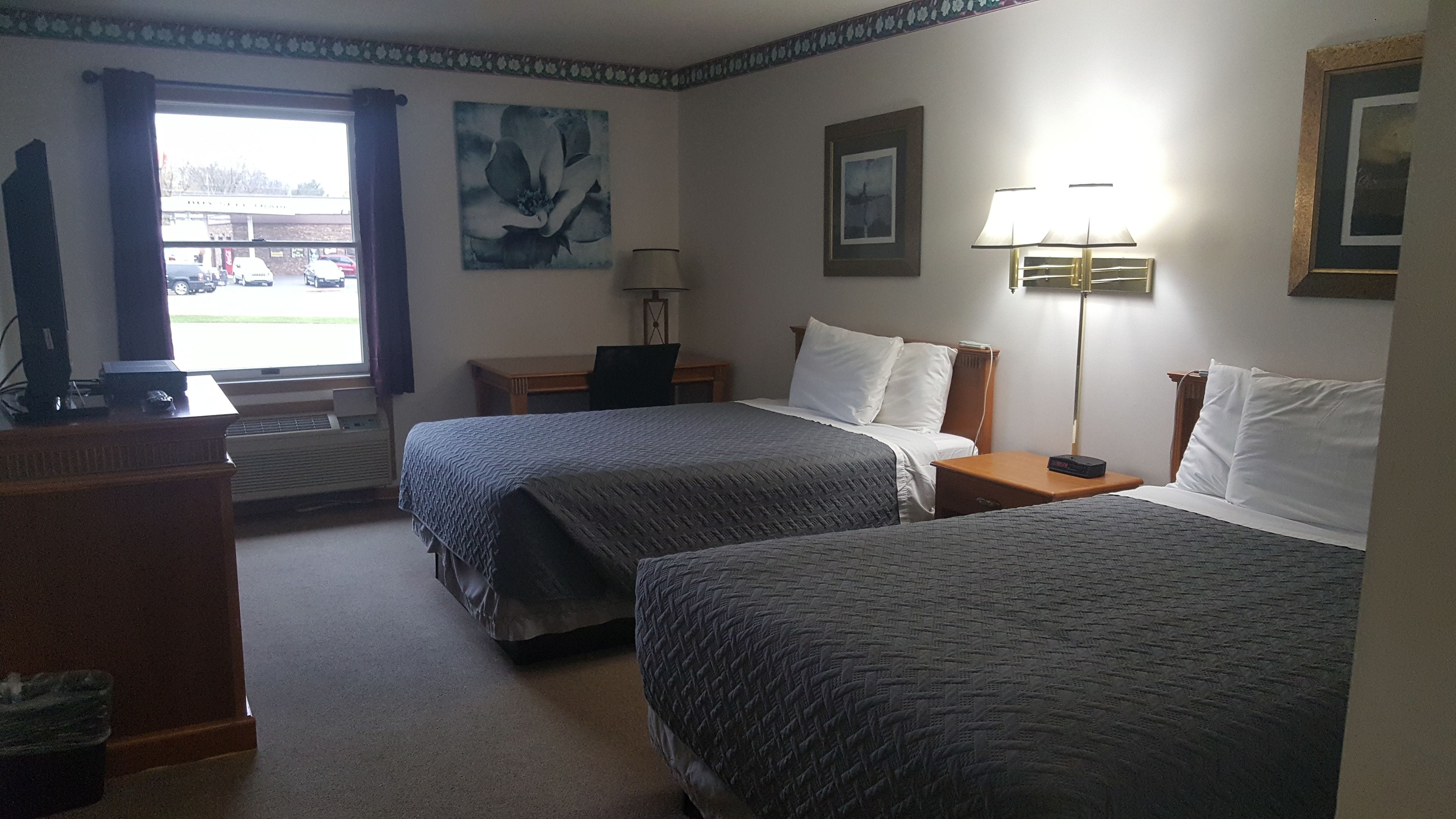 Habitación de hotel con dos camas, un escritorio, una silla, una lámpara y una ventana con cortinas.