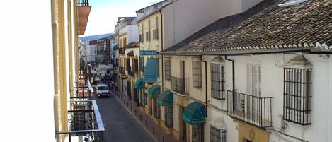 Una calle estrecha bordeada de edificios, algunos con balcones y otros con toldos.