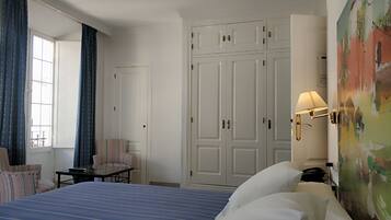 A hotel room with a large bed, a chair, a desk, and a wardrobe.