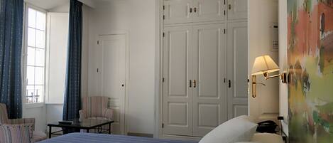 A hotel room with a large bed, a chair, a desk, and a wardrobe.