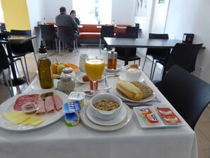 A breakfast table with plates of food, a glass of orange juice, and a bottle of olive oil. - Hotel Polo (Ronda)