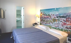 A hotel room with a bed, a nightstand with a lamp, a bathroom visible through an open door, and a colorful mural on the wall. - Hotel Polo (Ronda)