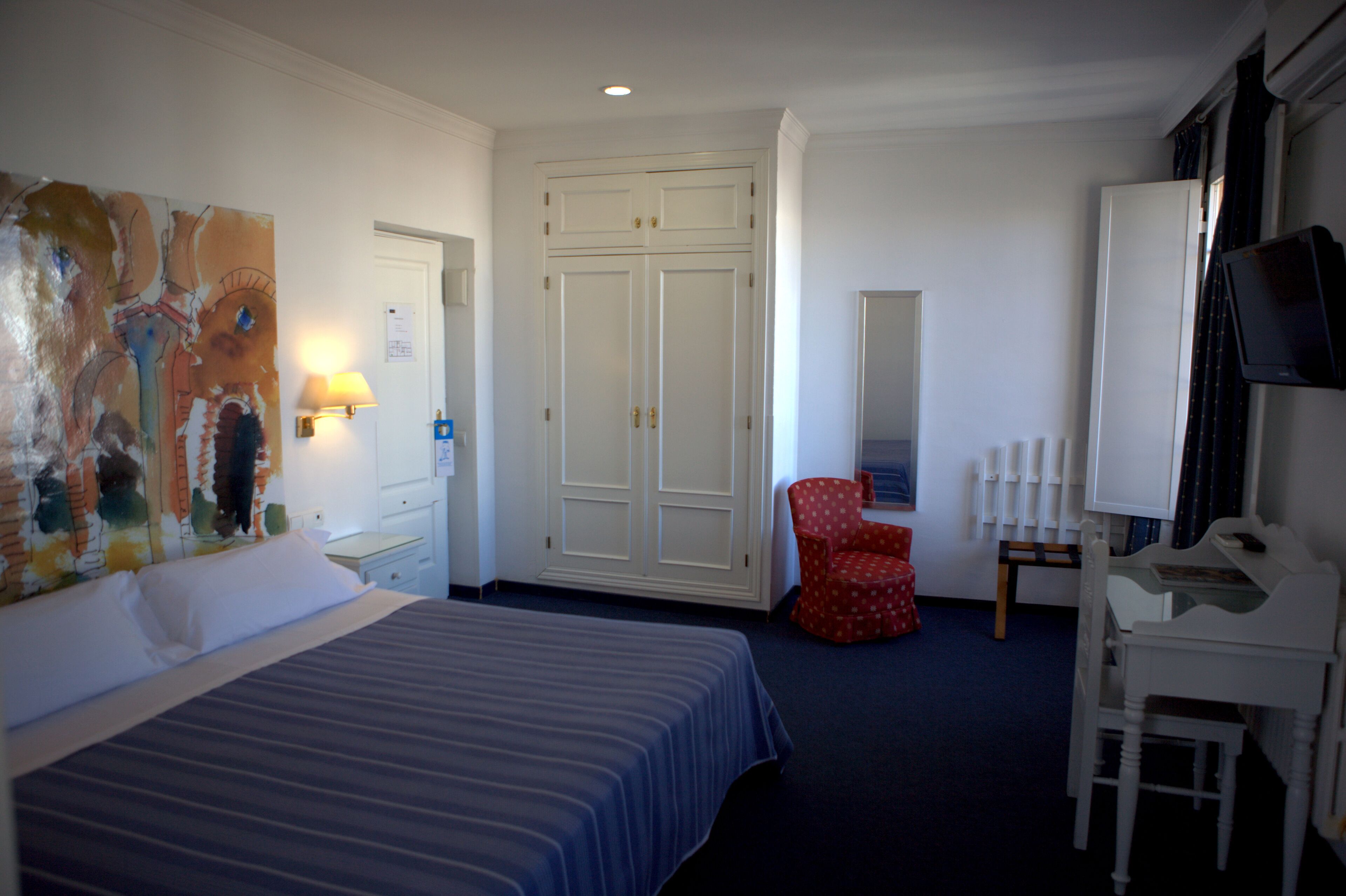 A hotel room with a bed, a desk, a chair, a wardrobe, and a television.