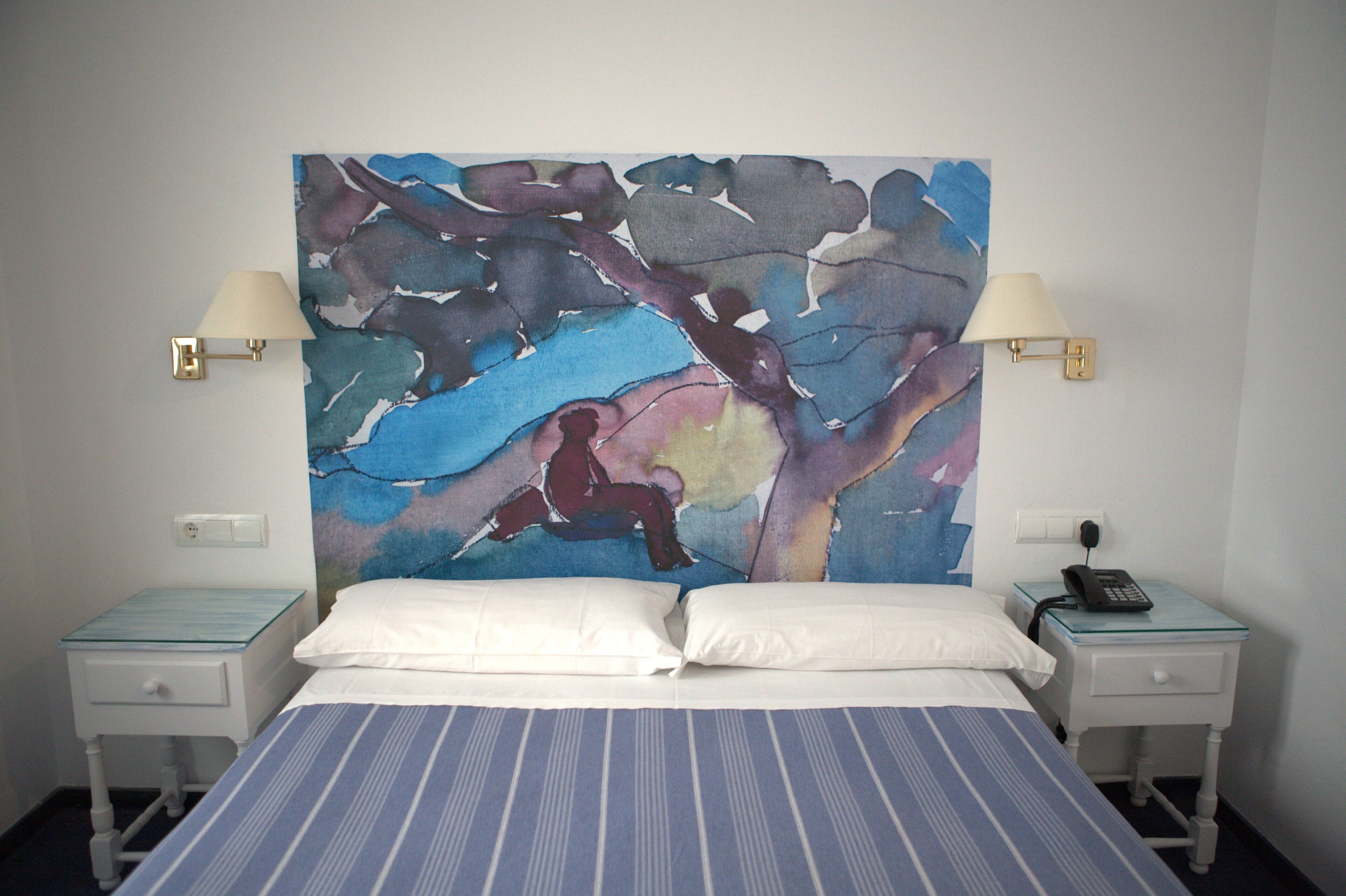 A hotel room with a bed, two bedside tables, a telephone, and a large abstract painting on the wall.