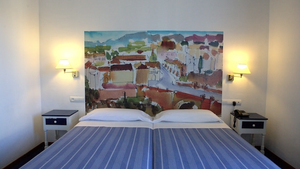 A hotel room with a bed, two bedside tables, and a colorful mural on the wall. - Hotel Polo (Ronda)