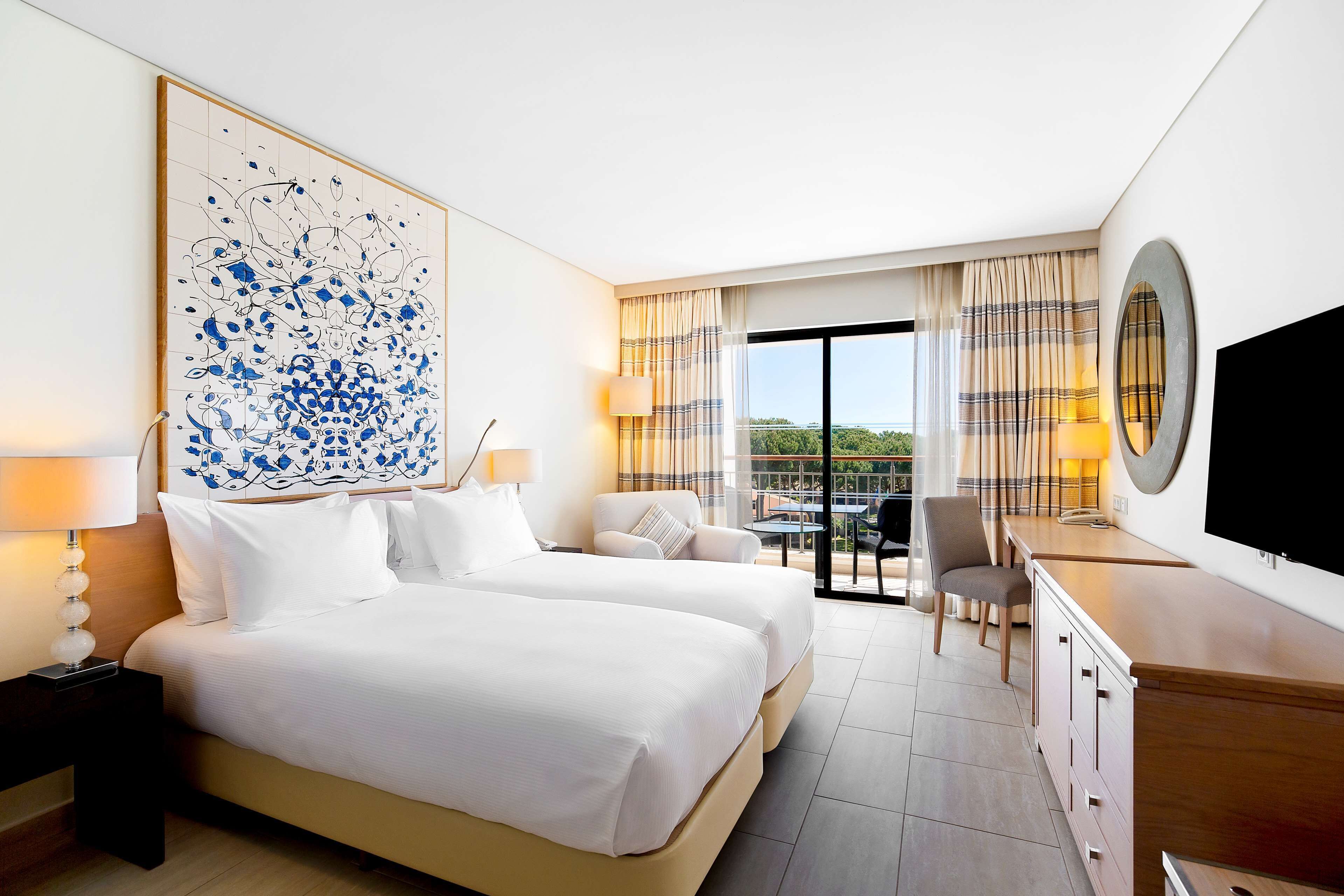 Habitación de hotel con dos camas, un escritorio, un televisor y un balcón con cortinas.