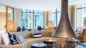 Un espacio lounge moderno con una chimenea grande, asientos cómodos y ventanas amplias que ofrecen vistas.