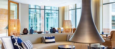 A modern lounge area with a large fireplace, comfortable seating, and large windows offering views.