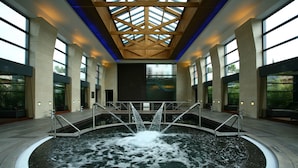 A large indoor pool with a central water feature, surrounded by high ceilings and large windows. - Hilton Vilamoura As Cascatas Golf Resort & Spa (Loulé)