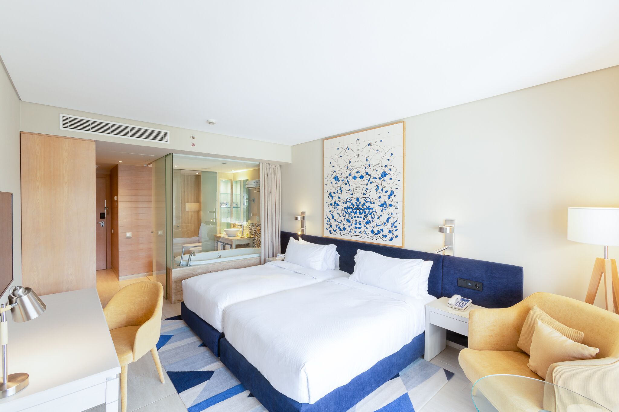 Habitación de hotel con una cama grande, un escritorio, una silla, una mesita de noche y una obra de arte colgada en la pared.