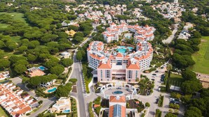 An aerial view of a resort with a central building featuring a swimming pool, surrounded by lush greenery and residential areas. - Hilton Vilamoura As Cascatas Golf Resort & Spa (Loulé)