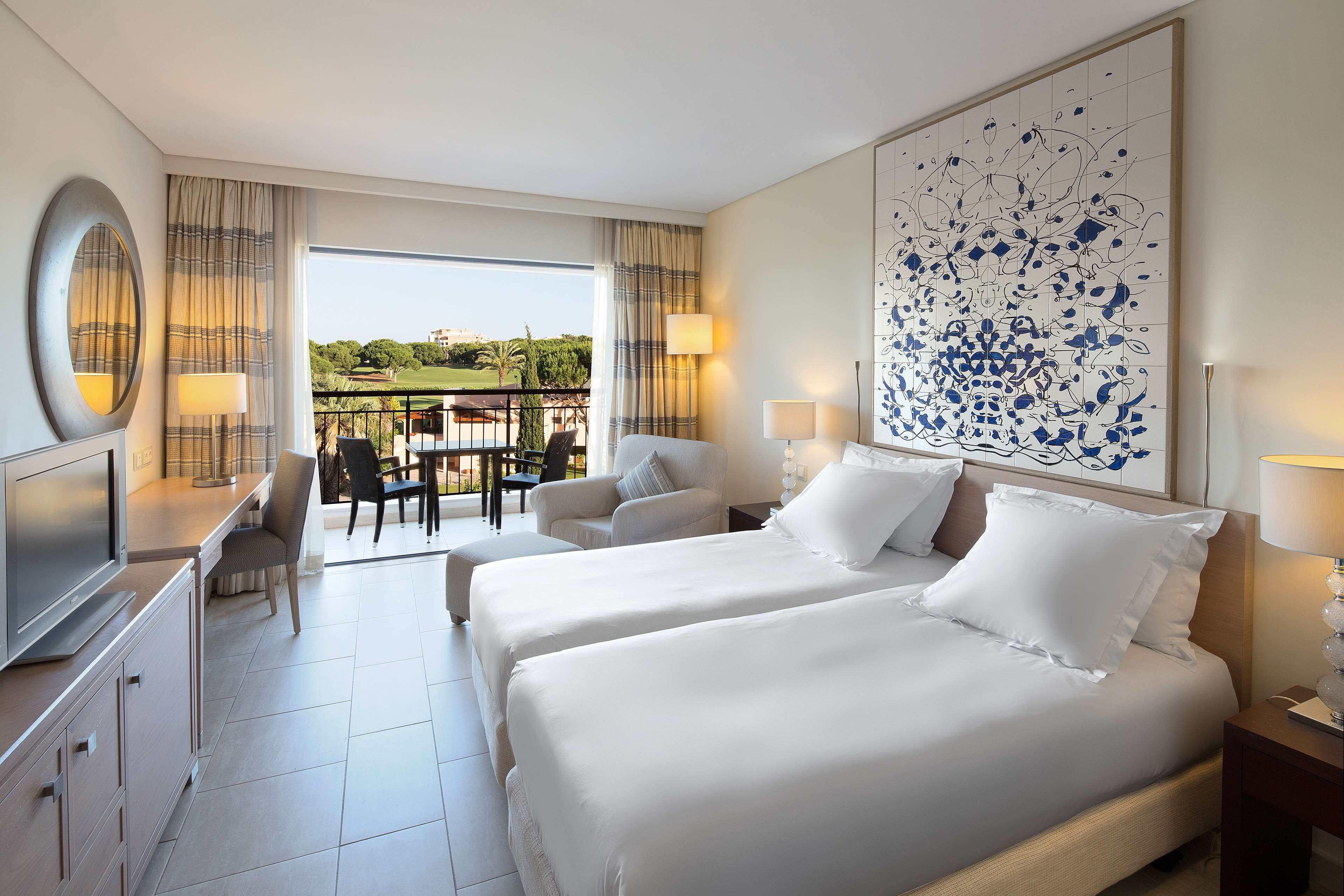 A hotel room with two beds, a desk, a chair, and a view of the outdoors.